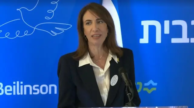 Woman speaks in front of blue backdrop which says "Beilinson"