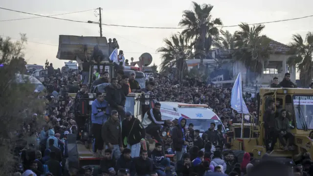 A crowd on a road. Some people are on top of vehicles.