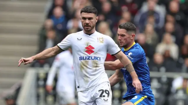 MK Dons' Scott Hogan plays the ball away from AFC Wimbledon's James Ball.