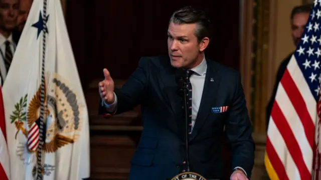 Pete Hegseth, wearing a dark blue suit and tie, stands at a podium soon after his swearing in as defence secretary