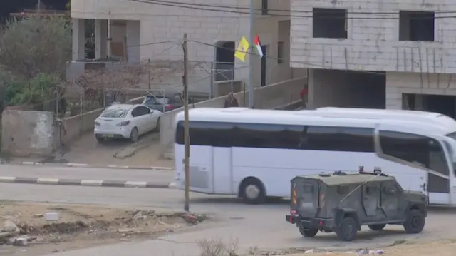 A white coach on a road alongside a military vehicle.