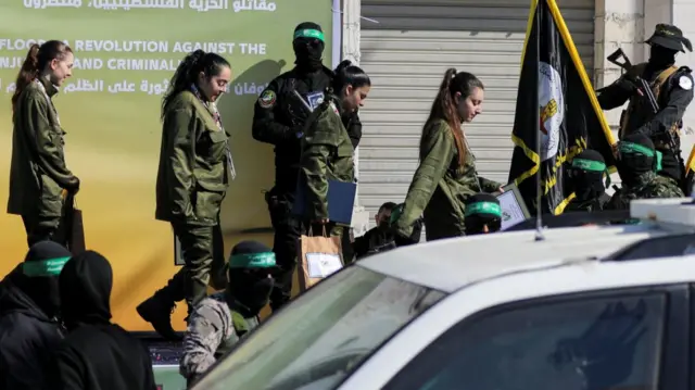 Female soldiers walking off stage after release. They're in green military uniforms holding paper bags