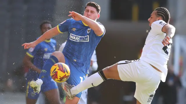 AFC Wimbledon's Matty Stevens and MK Dons' Nico Lawrence challenging for the ball