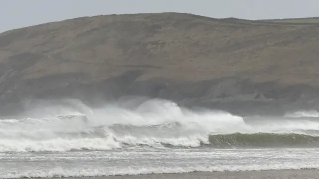 Choppy rows of waves seen with a cliff in the background.