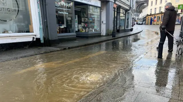 A shopping street covered in water with a man walking by.