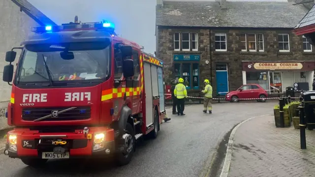 A road closed off with a fire engine at the front and buildings on the road behind.