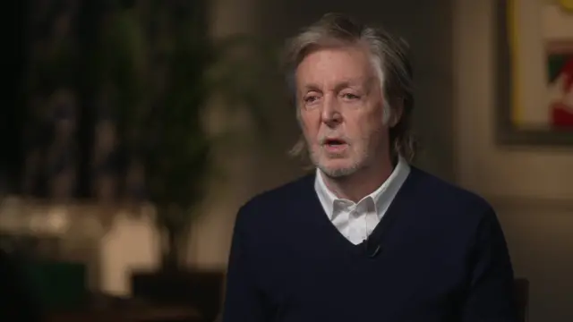 Sir Paul McCartney, photographed from chest up, wearing dark jumper and white collared shirt, speaking during an interview