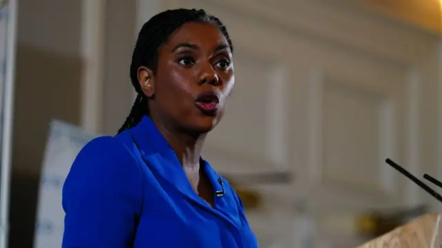 Kemi Badenoch at ledger delivers speech in blue dress, her head turning slightly to the right