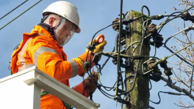 A picture of a engineer fixing a power line that was damaged during the storm.