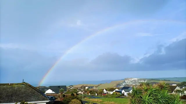 A rainbow seen with the sea and houses and fields below.