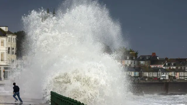 A person seen running away from a large wave crashing up onto the pathway by the seaside