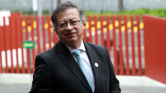 A bespectacled Gustavo Petro, wearing a black suit with a blue tie, stands outside