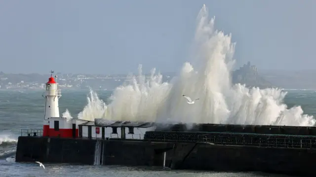 Waves crashing up onto the pier in Penzance with seagulls in the foreground