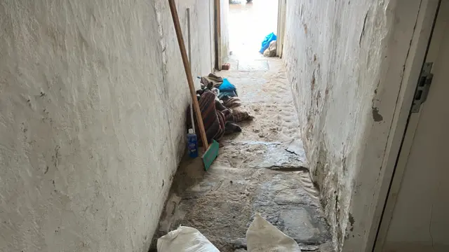 A hallway in a house that has dried up a little but has been visibly damaged by flood water