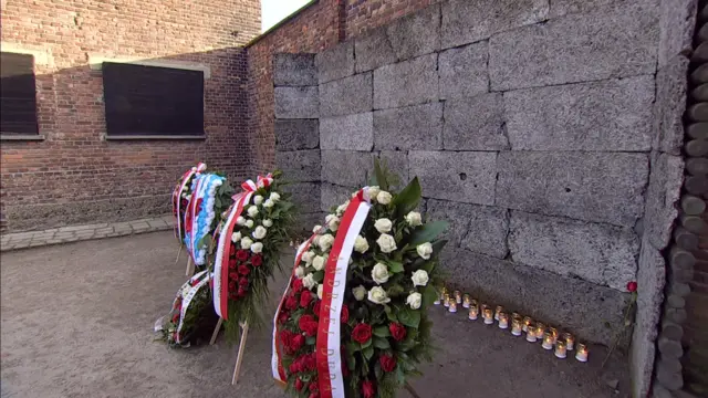 Candles at the base of the wall, with three large wreaths in front of them