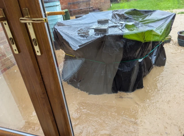 The picture taken from inside a house shows water building in a garden