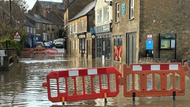 Red barriers block a flooded road outside of a Co-Op storefront