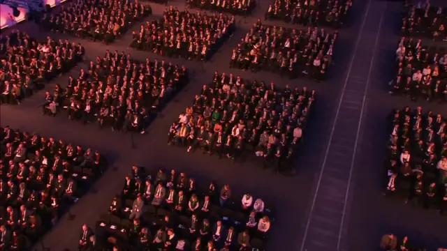 Large crowds of people sat on seats with gaps between different rows