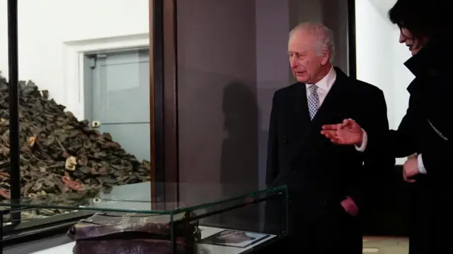 Charles looks at an exhibit of a pile of shoes and an old bag