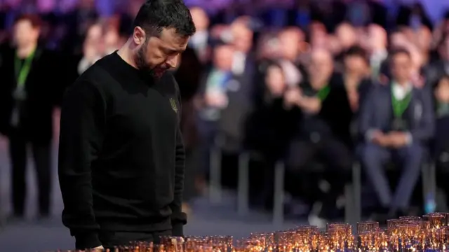 Ukrainian President Volodymyr Zelensky standing by the candles with his head bowed down