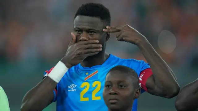 Chancel Mbemba, wearing the Congolese football kit at a match, makes a gesture expressing solidarity with the victims of DR Congo's conflict