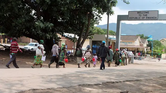 People walk across the border, under a sign that reads 'welcome to Rwanda'