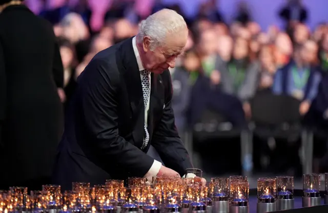 King Charles III in a suit laying a candle on a table full of lit candles