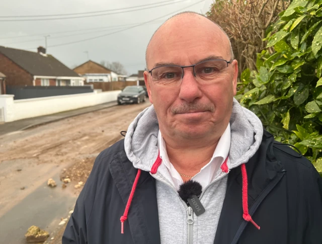 Mike Berry standing on a street in Chard.  Gravel and mud can be seen on the road in the background