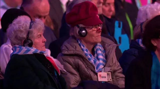 Two women wear headphones as they listen to the music