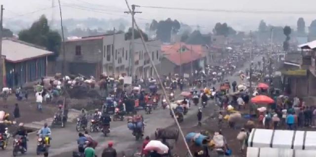 Long line of people walking and some on motorbikes seen along street in Goma