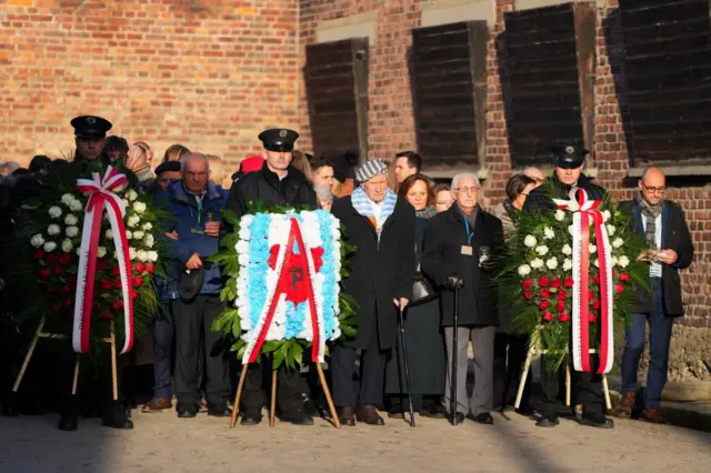 A row of people lined up behind three police officers holding wreaths