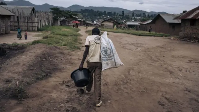 A man carries a bucket and a white sack, emblazoned with the worlds 'World Food Programme'