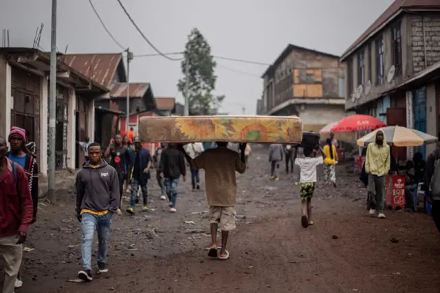 A man balances a mattress on his head walks down the streets of Goma