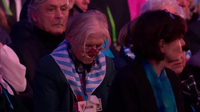 A woman in a blue and white striped scarf bows her head