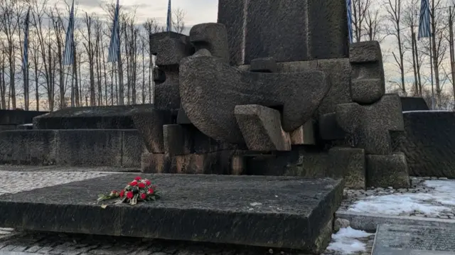 A memorial with red roses placed at the bottom. There is some snow on the ground