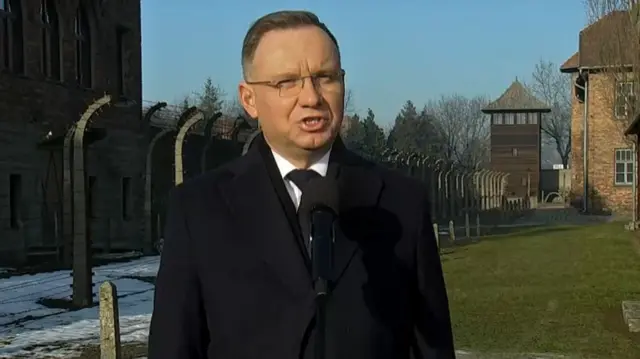 Duda speaking in front of a wire fence and a watch tower