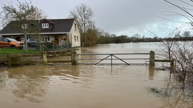 A farm house amidst brown flood water on a cloudy day