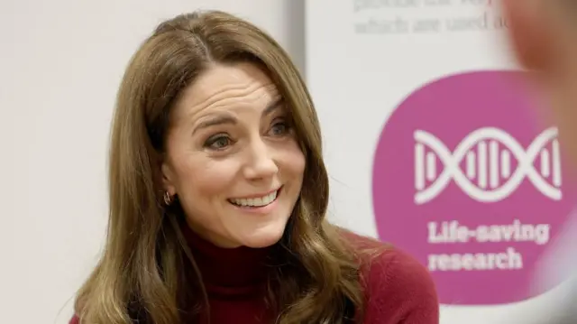 Close up shot of the Princess of Wales. Behind her a banner says Life-saving research in white lettering on a pink background