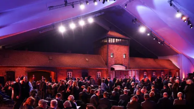 A tent full of people, lit up red, with a concrete building at the back and a wooden train car sitting in an archway of the building