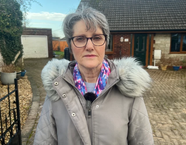 Chard resident Elaine Merrick-Reed standing infront of her house.  She is wearing a grey coat