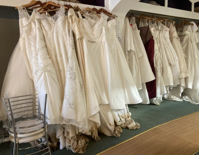 The picture shows dresses in a bridal shop. Brown stains from the floodwater can be seen at the bottom of them