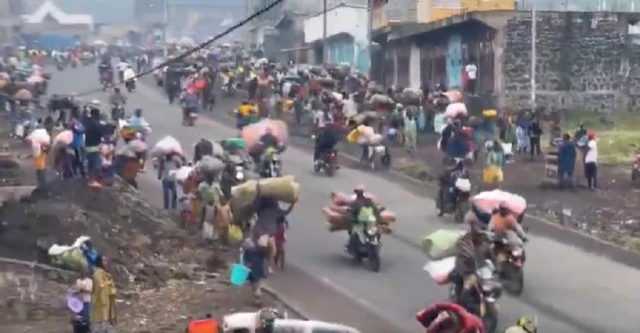 Road in Goma with people walking, some on motorcycles carrying their belongings