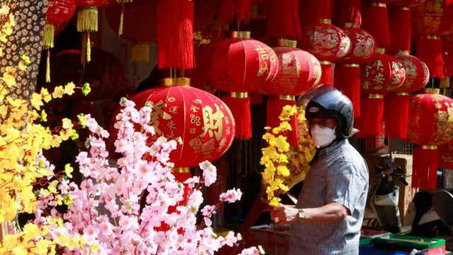 Man in motorcycle helmet and surgical mask standing near Chinese lanterns