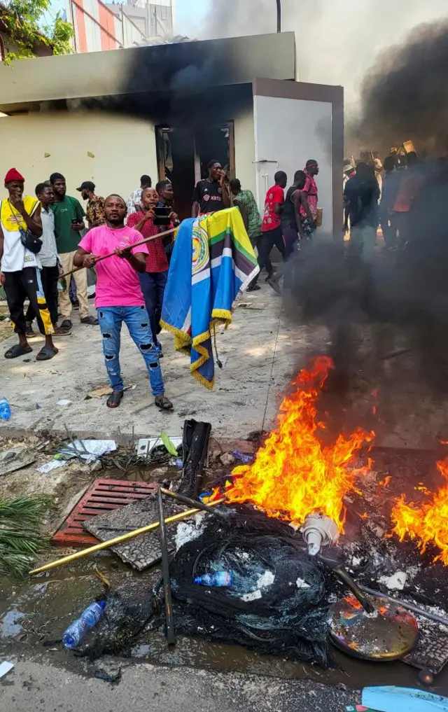 A protester prepares to burn the flag of EAC (East Africa Community) as Uganda's embassy gets looted in Kinshasa