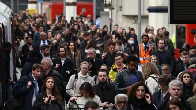 A dense crowd of people walk down a train station platform