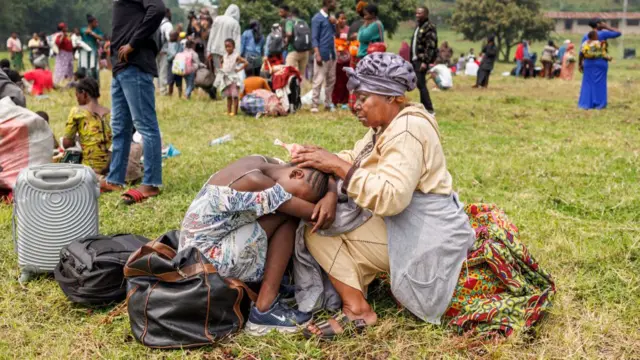 A girl rests her head on a woman's knees as others stand in the background at the Rugerero transit camp in Gisenyi