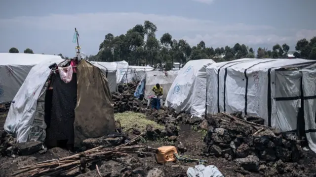 A man can be seen sitting between rows of white tents at Rubayo camp