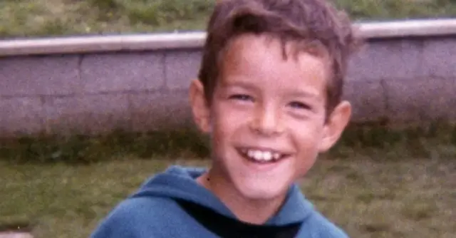 Sean Mclaughlin wearing a blue hoodie. He has short brown hair and is smiling at the camera. He is standing in a garden