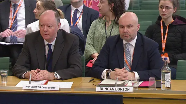 Prof Chris Whitty and Duncan Burton sit side-by-side at a wooden desk, before MPs sat in a horseshoe formation, answering questions put to them