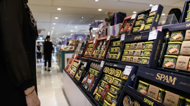 A shopper stands in front of cans of spam at a supermarket